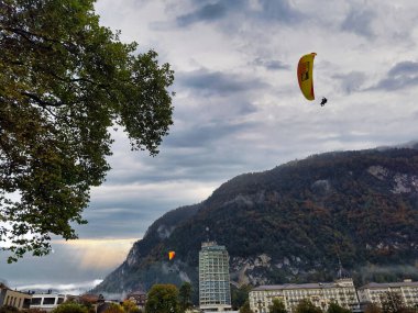 Sisli dağ manzarasıyla çevrili, yüksek bir binanın üstündeki sarı paraglider.