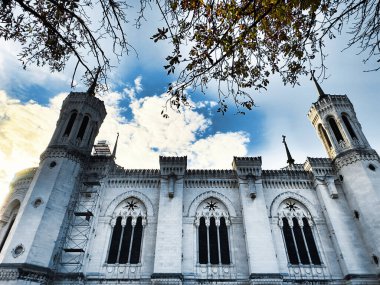 Historic church facade with gothic windows, branches, and cloudy sky clipart