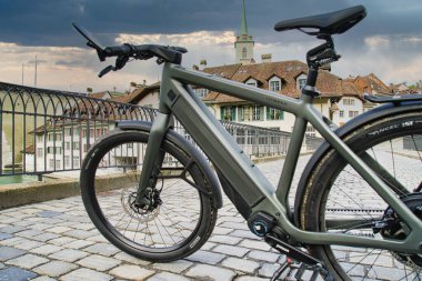 30.05.24. Bern, Swizerland. Üzerinde tarihi bir Avrupa kilisesi ve tarihi bir kasaba mimarisi olan kaldırım taşı köprüsü üzerinde parlak bir elektrikli bisiklet..