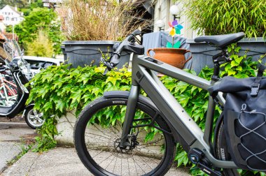 25,05,24. Bern, Swizerland. Yeşillik ve kentsel yerleşim yerlerindeki tarihi Avrupa tarzı evlerin yakınındaki kaldırıma park etmiş pannier çantalı elektrikli bir bisiklet.