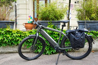 25,05,24. Bern, Swizerland. Yeşillik ve kentsel yerleşim yerlerindeki tarihi Avrupa tarzı evlerin yakınındaki kaldırıma park etmiş pannier çantalı elektrikli bir bisiklet.