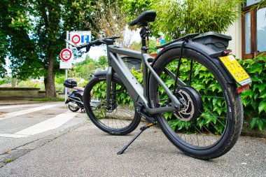 25,05,24. Bern, Swizerland. Yeşillik ve kentsel yerleşim yerlerindeki tarihi Avrupa tarzı evlerin yakınındaki kaldırıma park etmiş pannier çantalı elektrikli bir bisiklet.