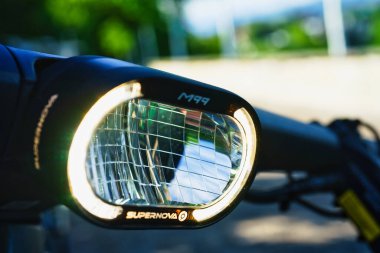 30.05.24.Berns.Wizerland. Yeşil ağaçlar ve mavi gökyüzünün yer aldığı bulanık doğal bir arka planı olan elektrikli bisiklet far ve gidonların yakın çekimi.