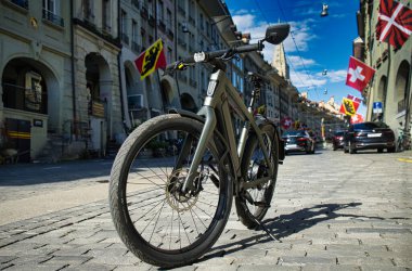 25,05,24.Bern, Swizerland. Parlak mavi gökyüzü altında klasik mimari ile çevrili tarihi bir Avrupa caddesinde elektrikli bisikletin alçak açılı görüntüsü.