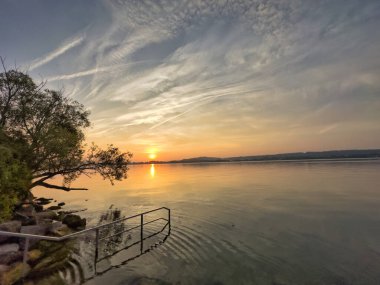 Bulutlu bir gökyüzünün altında sakin turkuaz suların üzerinde bir olta tutan bir elle balık tutma sahnesi huzurlu ve sakin bir atmosfer yaratıyor.