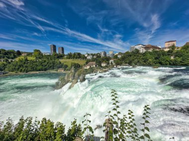 Güçlü bir şelale, uçurumlar ve yeşil gökyüzü altında yükselen sis ile dinamik ve dramatik bir manzara yaratıyor. Rhine Falls.