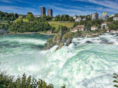 Güçlü bir şelale, uçurumlar ve yeşil gökyüzü altında yükselen sis ile dinamik ve dramatik bir manzara yaratıyor. Rhine Falls.