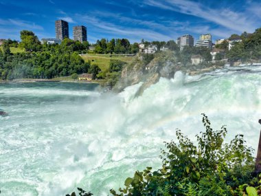 Güçlü bir şelale, uçurumlar ve yeşil gökyüzü altında yükselen sis ile dinamik ve dramatik bir manzara yaratıyor. Rhine Falls.