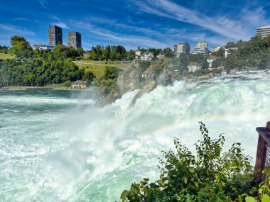Güçlü bir şelale, uçurumlar ve yeşil gökyüzü altında yükselen sis ile dinamik ve dramatik bir manzara yaratıyor. Rhine Falls.