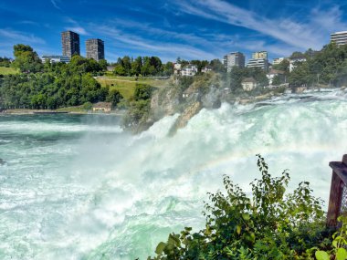 Güçlü bir şelale, uçurumlar ve yeşil gökyüzü altında yükselen sis ile dinamik ve dramatik bir manzara yaratıyor. Rhine Falls.
