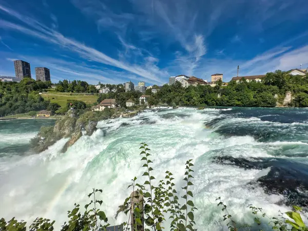 Güçlü bir şelale, uçurumlar ve yeşil gökyüzü altında yükselen sis ile dinamik ve dramatik bir manzara yaratıyor. Rhine Falls.
