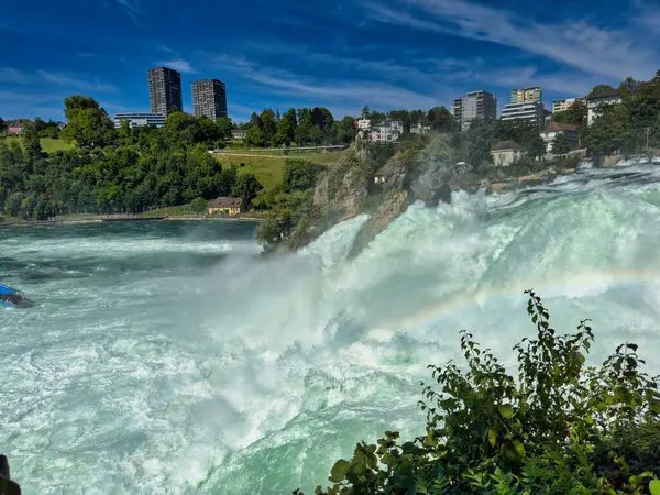 Güçlü bir şelale, uçurumlar ve yeşil gökyüzü altında yükselen sis ile dinamik ve dramatik bir manzara yaratıyor. Rhine Falls.