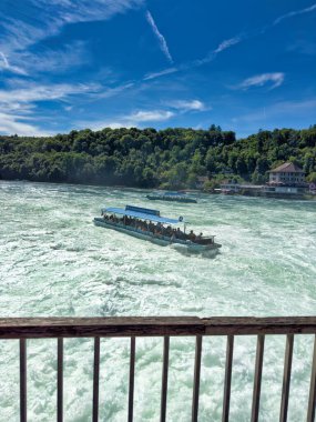 Güçlü bir şelale, uçurumlar ve yeşil gökyüzü altında yükselen sis ile dinamik ve dramatik bir manzara yaratıyor. Rhine Falls.