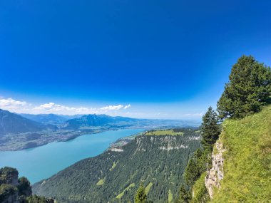 Sarp kayalıklarla, yemyeşil yemyeşil yemyeşil ve parlak mavi gökyüzünün altındaki görkemli dağ zirveleriyle çevrili turkuaz bir alp gölü nefes kesici.