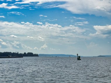 Sakin sularla huzurlu göl manzarası, uzak bir heykel ve parçalı bulutlu bir gökyüzünün altında sakin bir ufuk.