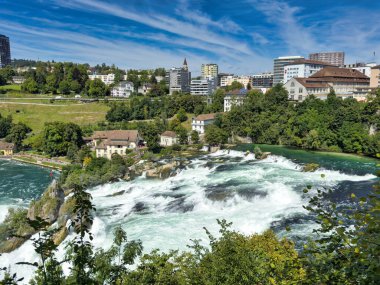 Güçlü bir şelale, uçurumlar ve yeşil gökyüzü altında yükselen sis ile dinamik ve dramatik bir manzara yaratıyor. Rhine Falls.
