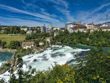 Güçlü bir şelale, uçurumlar ve yeşil gökyüzü altında yükselen sis ile dinamik ve dramatik bir manzara yaratıyor. Rhine Falls.