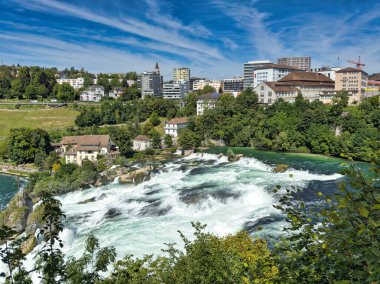 Güçlü bir şelale, uçurumlar ve yeşil gökyüzü altında yükselen sis ile dinamik ve dramatik bir manzara yaratıyor. Rhine Falls.