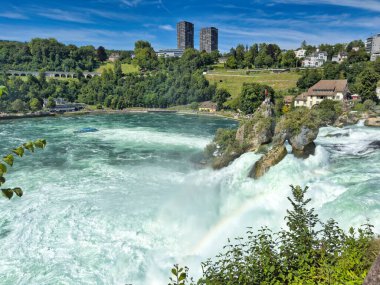 Güçlü bir şelale, uçurumlar ve yeşil gökyüzü altında yükselen sis ile dinamik ve dramatik bir manzara yaratıyor. Rhine Falls.