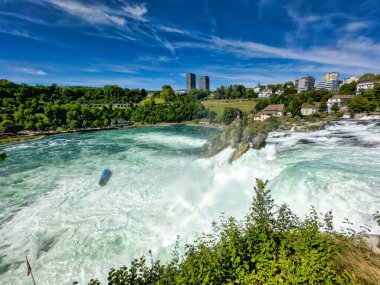Güçlü bir şelale, uçurumlar ve yeşil gökyüzü altında yükselen sis ile dinamik ve dramatik bir manzara yaratıyor. Rhine Falls.