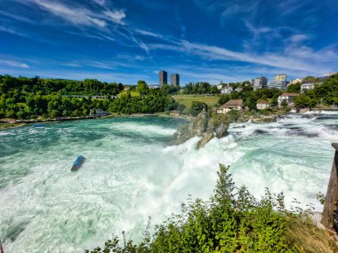 Güçlü bir şelale, uçurumlar ve yeşil gökyüzü altında yükselen sis ile dinamik ve dramatik bir manzara yaratıyor. Rhine Falls.