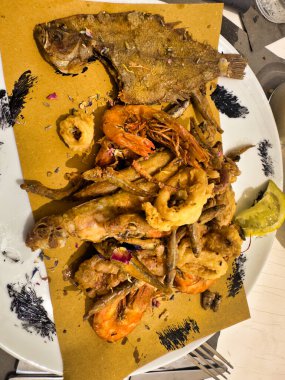 A plate of mixed fried seafood with shrimp, calamari, and fish, garnished with lemon clipart