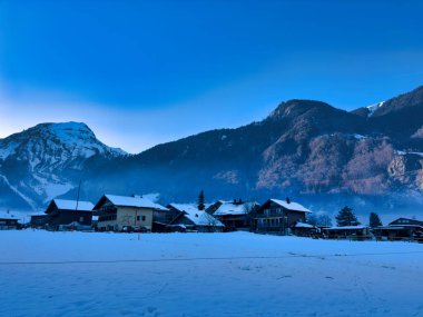 Kır evleri ve açık mavi gökyüzü altında dağları olan karlı bir köy.