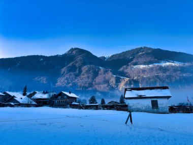 Kır evleri ve açık mavi gökyüzü altında dağları olan karlı bir köy.