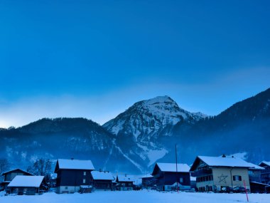 Kır evleri ve açık mavi gökyüzü altında dağları olan karlı bir köy.