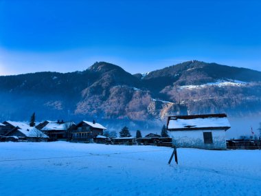 Kır evleri ve açık mavi gökyüzü altında dağları olan karlı bir köy.