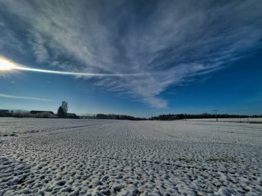 Parlak güneş ve açık mavi gökyüzü altında karla kaplı bir arazi.