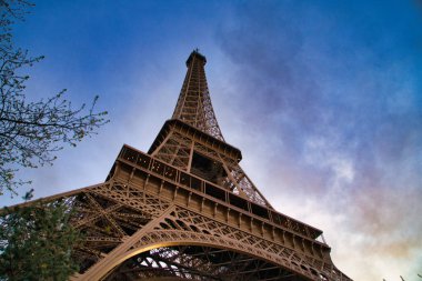 Paris 'teki Eyfel Kulesi' nin manzarası ilkbahar yeşili ağaçlarla çevrelenmiş mavi gökyüzüne karşı