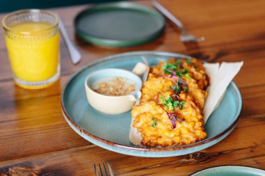 Sos soslu bir tabak kızarmış yemek ahşap bir masada oturur. Masada bir bardak portakal suyu da var. Sahne günlük ve rahat bir atmosfer sunuyor, yemek gibi.