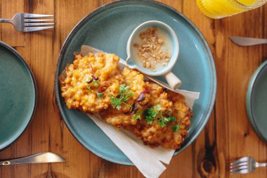 Yanında sos olan bir tabak kızarmış yemek ahşap bir masada oturur. Masa çatal, bıçak ve kaşıkla hazırlandı ve masada iki kase var. Sahne sıradan ve davetkar.