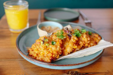 Bir tabak kızarmış mısır cipsi ve bir bardak portakal suyu. Tabak ahşap bir masanın üzerinde.