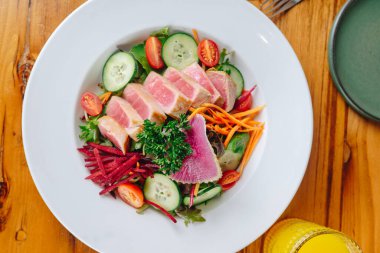 Sebze ve et salatası ile birlikte beyaz bir tabak. Tabak ahşap bir masanın üzerinde. Salata renkli ve iştah açıcı.