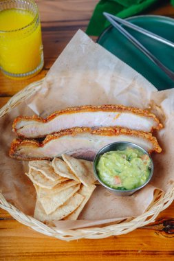 Guacamole soslu bir tabak et ve patates kızartması. Tabak ahşap bir masanın üzerinde ve arka planda bir bardak portakal suyu var.