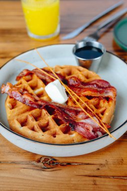Bir tabak domuz pastırması ve bir bardak portakal suyu ile waffle. Tabak ahşap bir masanın üzerinde.