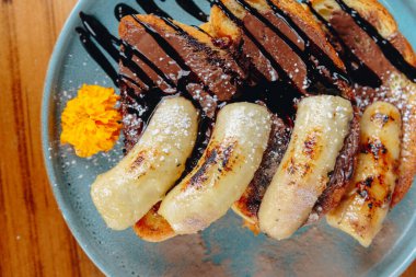 Üstünde muz ve çikolata sosu olan bir tabak yemek.