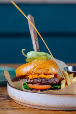 Üstünde turşu mızrağı olan bir hamburger. Hamburger, yanında patates kızartması olan beyaz bir tabakta servis edilir.