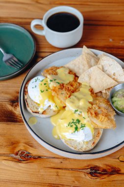Yanında patates kızartması ve bir fincan kahve olan bir tabak yemek. Tabağın üzerinde sarı sos ve yanında da cips var.