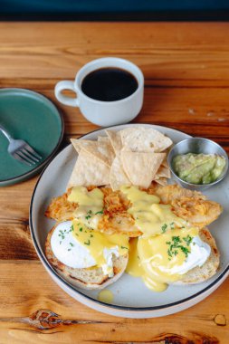 Yanında cips ve guacamole olan bir tabak yemek ahşap bir masada oturur. Masada bir fincan kahve de mevcuttur. Yemek tabağı, yumurta ve tosttan oluşan bir kahvaltı tabağıdır.