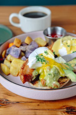 Sandviç, patates ve yumurtalı bir tabak yemek. Tabak ahşap bir masanın üzerinde.