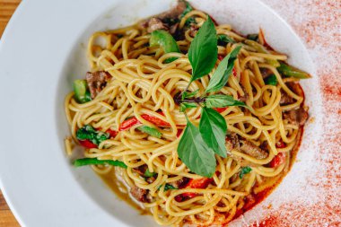 Bir kase etli ve sebzeli erişte. Eriştenin üstünde yeşil bir yaprak var.