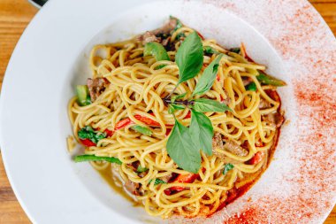 Bir kase etli ve sebzeli erişte. Eriştenin üstünde yeşil bir yaprak var.