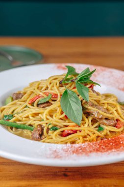 Bir tabak etli ve sebzeli erişte. Tabak beyaz ve masa kahverengi.