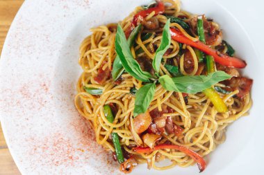 Sebzeli ve etli bir tabak erişte. Erişteler kırmızı sosla kaplanmış ve yeşil fesleğen yapraklarıyla kaplanmış.