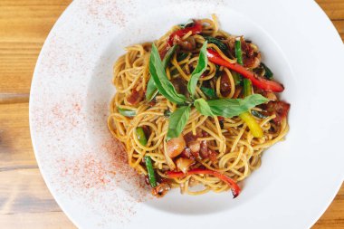 Bir tabak etli ve sebzeli erişte. Erişteler kırmızı sosla kaplanmış ve yeşil fesleğenle kaplanmış.