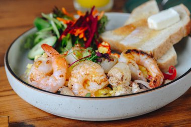 Karides ve sebzeli bir tabak yemek. Tabak ahşap bir masanın üzerinde. Yemekler lezzetli ve sağlıklı görünüyor.