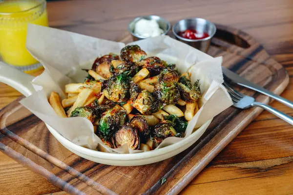 A plate of food with a fork and knife on a wooden table. The plate contains broccoli and fries
